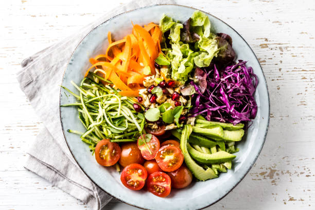Vegan buddha bowl. Bowl with fresh raw vegetables - cabbage, carrot, zucchini, lettuce, watercress salad, tomatoes cherry and avocado, nuts and pomegranate stock photo
