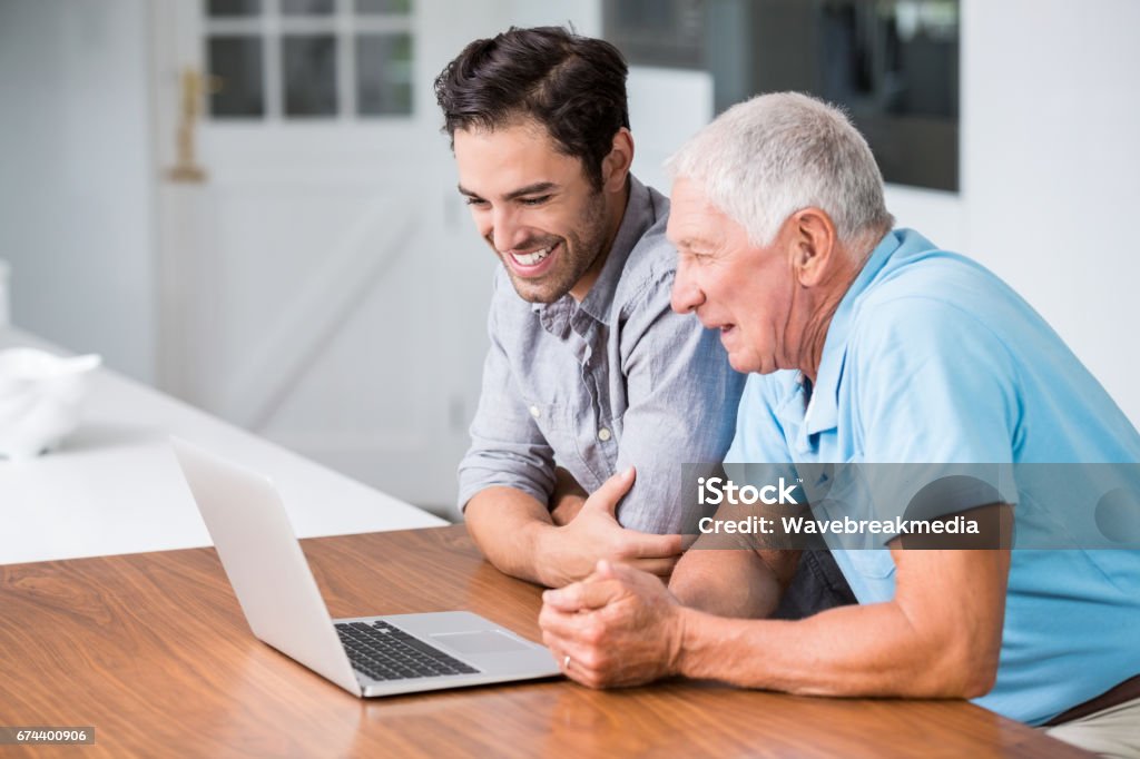 Smiling father and son using laptop Smiling father and son using laptop while sitting at desk Senior Men Stock Photo