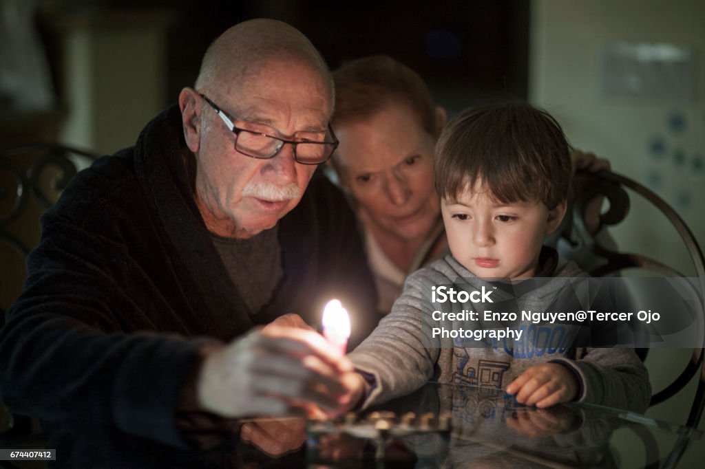 Jewish Family lighting Hanukkah Candles in a menorah for the holidays Jewish Family with granparents and grandson lighting Hanukkah Candles in a menorah for the holidays Judaism Stock Photo