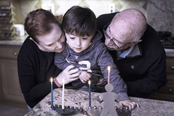familia judía con granpadres y nieto iluminando velas de hanukkah en una menorah para las vacaciones - enzo fotografías e imágenes de stock