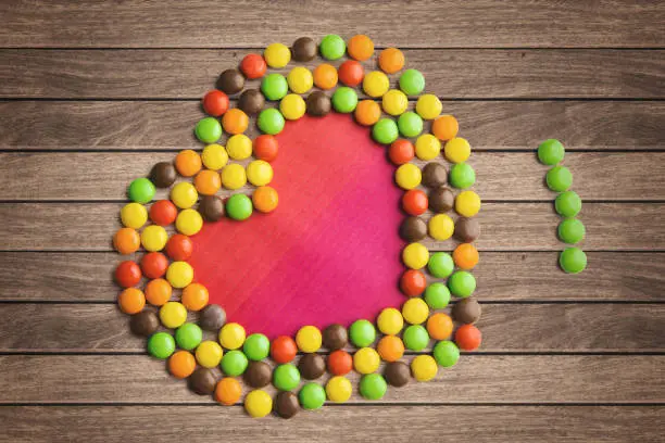 Image of colorful candies shaped a heart symbol on the wooden background