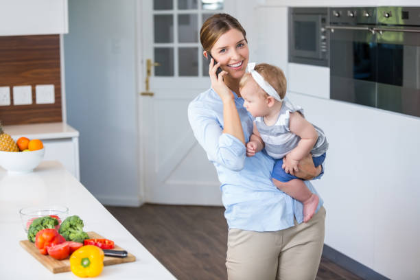 istock Woman talking on cellphone carrying daughter by kitchen counter 674431102