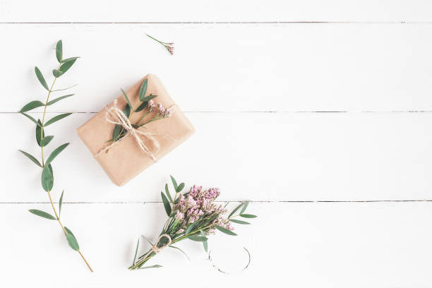 Gift, pink flowers and eucalyptus branches on white wooden background