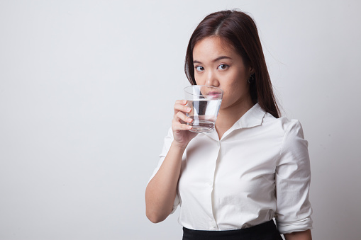 Young Asian woman with a glass of drinking water on white background