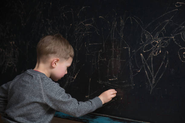 istock Back view of male elementary school student writes on the Blackboard 674452544
