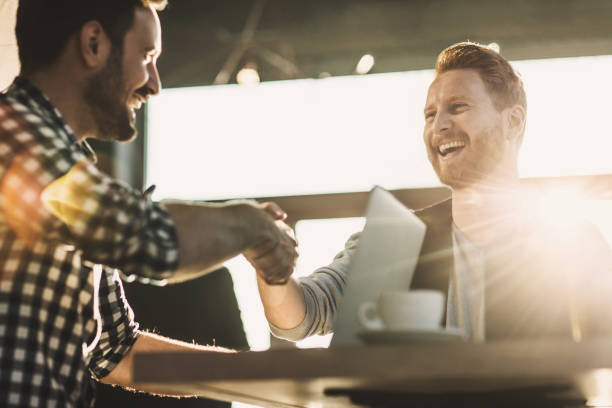 We have a deal! Happy red-haired businessman shaking hands with his colleague in a cafe. Focus is on redhead man. male friendship stock pictures, royalty-free photos & images