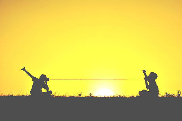 Silhouette Of Two Children With Tin Can Phones At Sunset  toy phone stock pictures, royalty-free photos & images