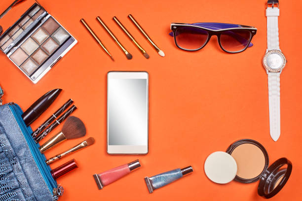 istock Flat lay, top view feminine table desk isolated on white. Workspace with cosmetics, phone, glasses, lipstick, nail lacquer, watches, mascara and eyeshadow in gold. Golden and black tones. 674500566