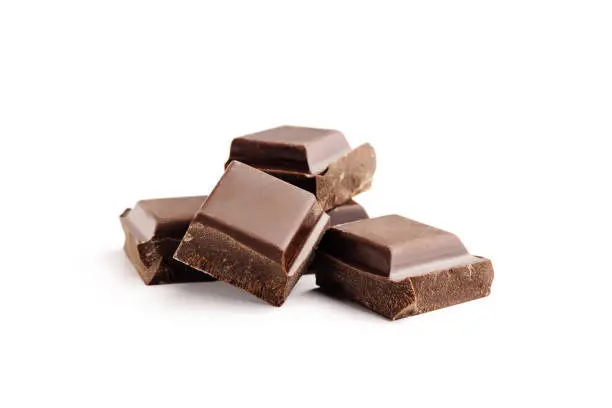 Pieces of bitter, dark chocolate bar, cubes on heap, isolated on white background, close-up view.