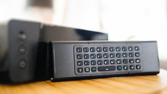 Full keyboard on small remote control next to wireless tv box used for TV Internet Telephone communication via fiber optic or coaxial cable