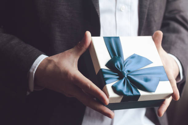 istock Man in suit offering gift with blue ribbon 674505902
