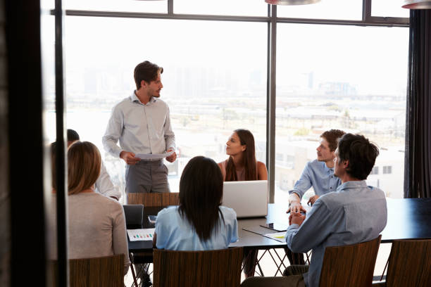 istock Young man with documents addresses team at boardroom meeting 674555272