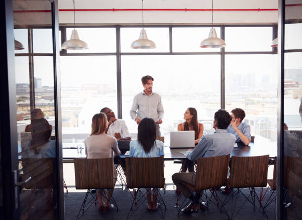 istock Young man stands addressing team at a meeting in a boardroom 674555280