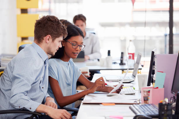 istock Young man and woman working together in an open plan office 674555410