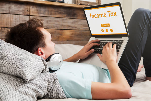 istock Man doing Income tax declaration on a website with a laptop while lying on the bed at home. 674558894
