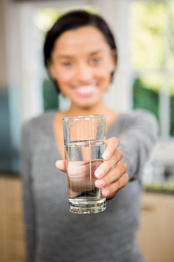 Smiling brunette holding glass of water in the kitchen