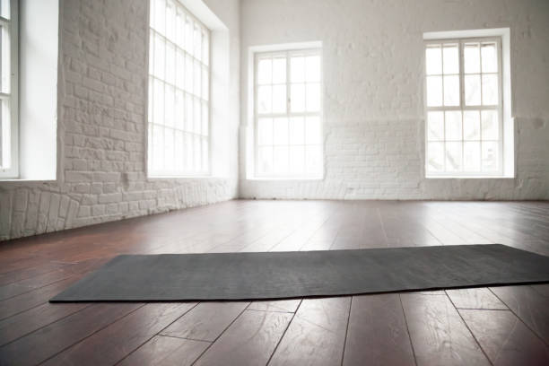 Empty white space, loft studio, yoga mat on the floor Empty white space in fitness center, white brick walls, natural wooden floor and big windows, modern loft studio, unrolled yoga mat on the floor, comfortable open area for sport and exercises yoga studio stock pictures, royalty-free photos & images