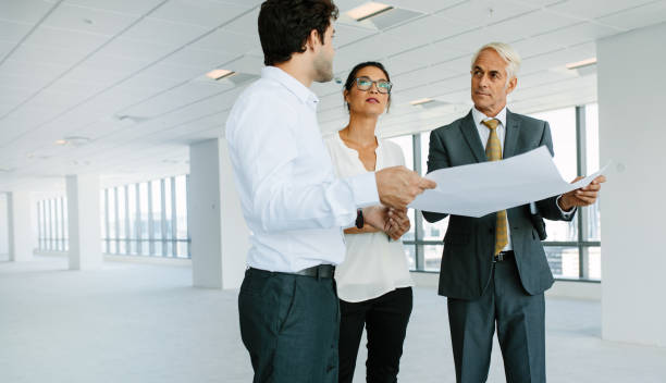 istock Estate broker discussing blueprints of new office space with clients 674570954