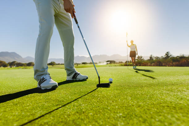 ゴルフ場で旗を掲げる女性パートナーとボールを置くゴルファー - golf golf course putting men ストックフォトと画像