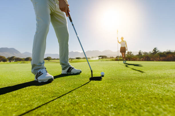 golfer que põr a esfera com a bandeira fêmea da terra arrendada do sócio no campo de golfe - golf flag putting green sport - fotografias e filmes do acervo