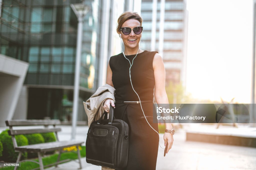 Listen to my favorite music after work Elegant strong business woman is walking in business district and using phone . She is 34 years old manager of company. She is happy and relaxed talking on her phone with headset Headphones Stock Photo