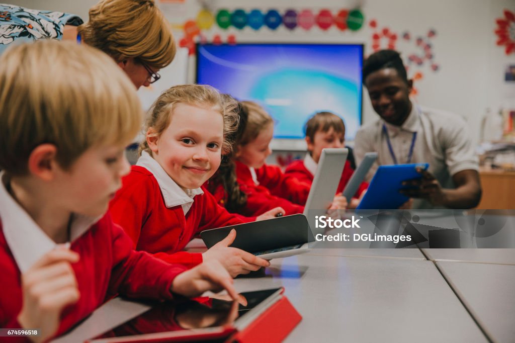 Happy Student In Technology Lesson Primary school children are in the ckassroom, learning about and using digital tablets. One of the girls is smiling at the camera. Classroom Stock Photo