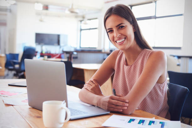 istock Young woman in office using laptop computer smiles to camera 674627800