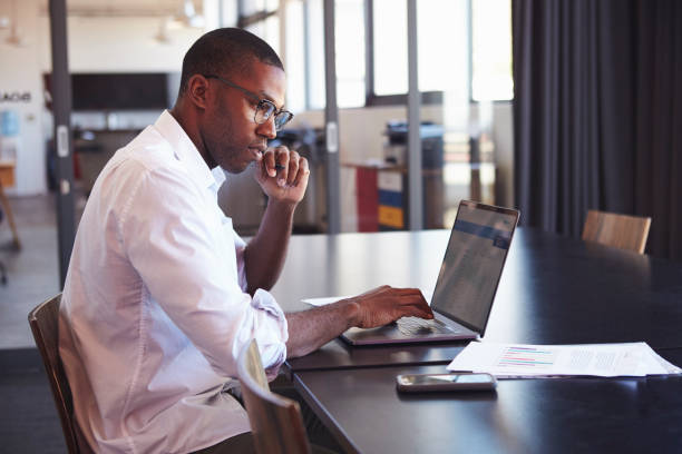 istock Young black man in wearing glasses using laptop in office 674627826