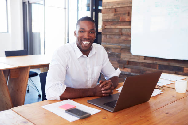 istock Young black man at desk with laptop computer looks to camera 674627838