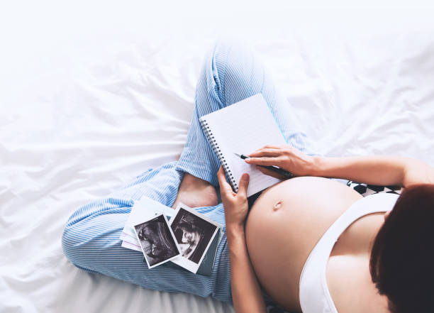 istock Pregnant woman makes notes in notebook and holding ultrasound image and medical documents 674638896