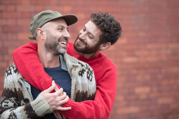 Gay couple cuddling and laughing in front of brick wall Gay couple hanging out gay man stock pictures, royalty-free photos & images