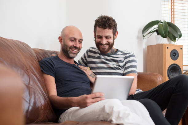 istock Gay couple sat cuddling on sofa, sharing tablet 674640246