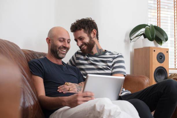 Gay couple sat cuddling on sofa, sharing tablet