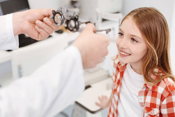 Sweet charming girl excited about fixing her eyesight Just an example. Emotional enthusiastic young lady trying on special diopters for picking the right lenses while paying a visit to her doctor myopia stock pictures, royalty-free photos & images