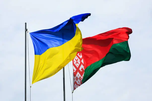 Symbol of friendship and partnership. Waving flags of Ukraine and Belarus on flagpoles against the sky