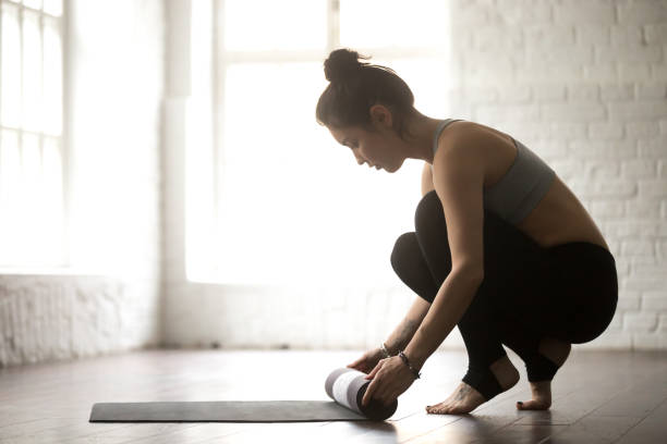 giovane donna attraente srotolando tappetino da yoga, bac studio loft bianco - unrolling foto e immagini stock