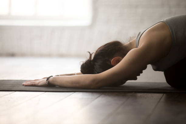 Young attractive sporty yogi woman practicing yoga concept, sitting in Child exercise, Balasana pose, working out, wearing sportswear, close up, white loft studio background, side view