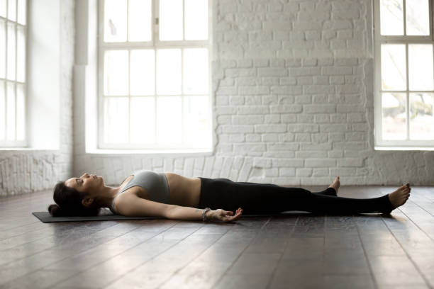 mujer joven atractiva en savasana pose, blanco loft studio backg - lying on back fotos fotografías e imágenes de stock