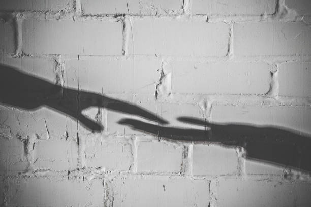 istock Imitation. Dark shadows of hands reaching to each other on the bricks wall background. 674675314