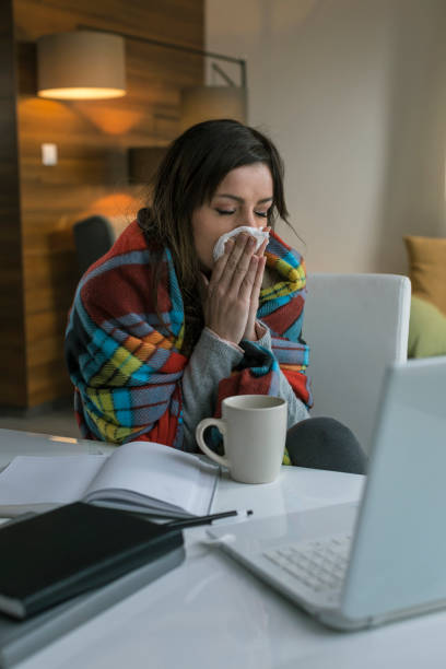 istock Young woman sneezes while working from home on a laptop 674687444