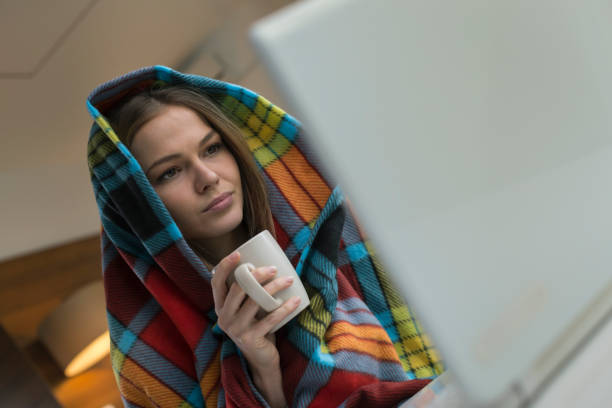 Woman which has a flu holding cup of tea and working from home on a laptop stock photo