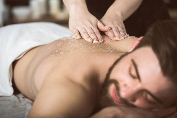 Man relaxing during a salt scrub beauty therapy Man at beautician's getting an exfoliating massage with salt peeling exfoliation stock pictures, royalty-free photos & images