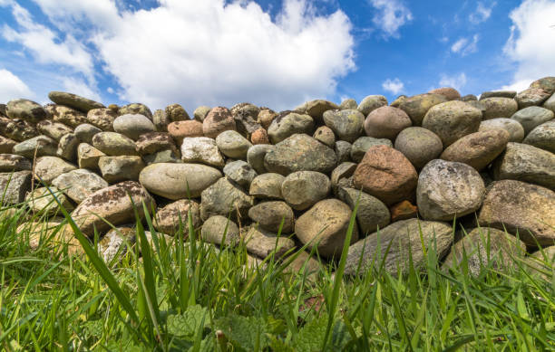 istock Old Stone wall with green grass in front and blue sky with clouds above 674753224