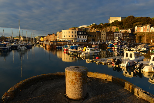 Wide angle image of the Old and English harbor just down the road from the town centre, occupied by small local boats and the water edge lined by local businesses, a 19th century small port now replaced by a new harbor and modern industry out of shot.