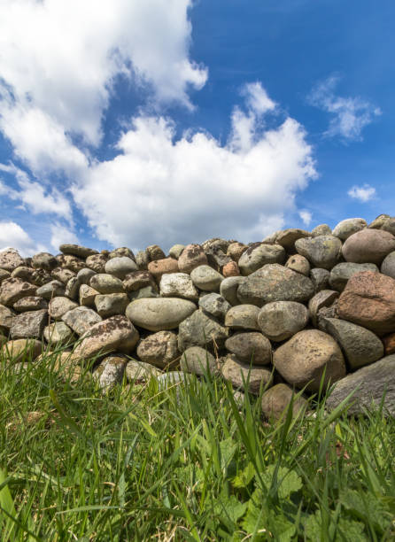 istock Old Stone wall with green grass in front and blue sky with clouds above, vertical image 674753702