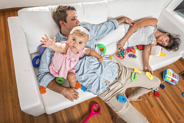 Babies and parenting Life This is a photo relating to the stress of parenting and having children by showing all the Best thing chaos in the home and the parents being exhausted and sleeping overworked funny stock pictures, royalty-free photos & images