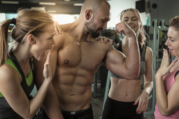 Three women admiring mens big muscles at gym Three young women admiring mens big muscles at gym people laughing hard stock pictures, royalty-free photos & images