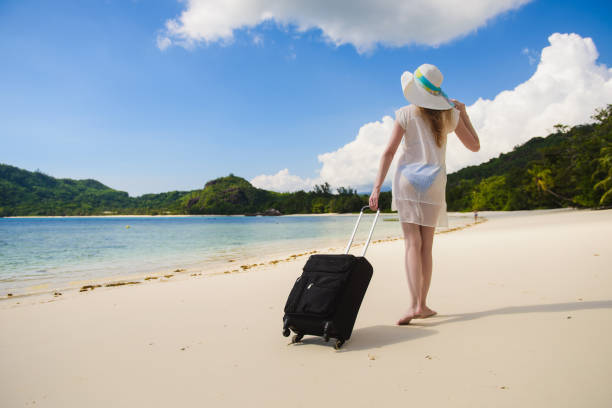 istock Woman with suitcase and swimsuit at beach 674759900