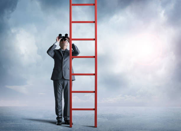 istock Businessman Looking Through Binoculars Looks Up At Tall Ladder 674762890
