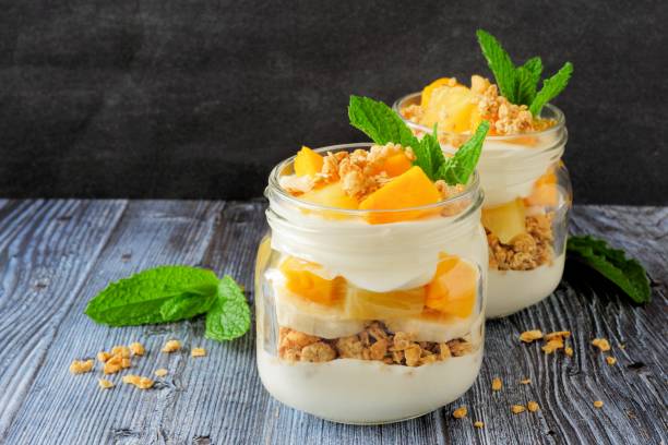 Mango, pineapple parfaits in mason jars on dark background